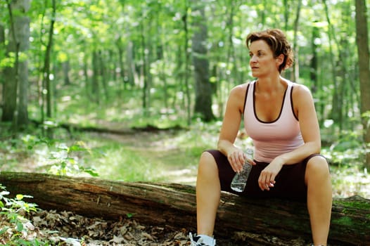 Mature woman runner resting in woods.