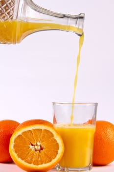 Orange juice being poured into a glass surrounded by orange fruits
