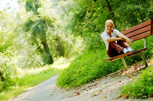 Pretty young girl sitting on a bench in the forest.