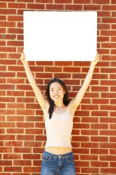 Fashionable girl with blank white poster against brick wall.