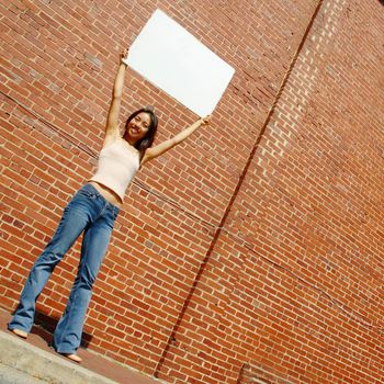 Fashionable girl with blank white poster against brick wall.