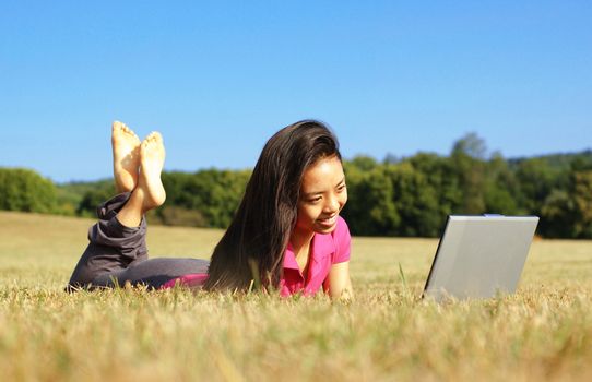 Fashionable girl working on laptop in a meadow.