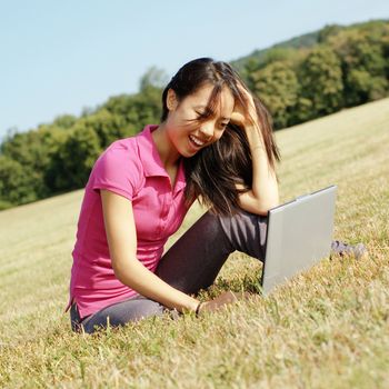 Fashionable girl working on laptop in a meadow.