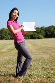 Girl with blank sign standing in a field.