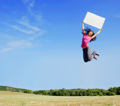 Girl jumping with a blank sign in a field.