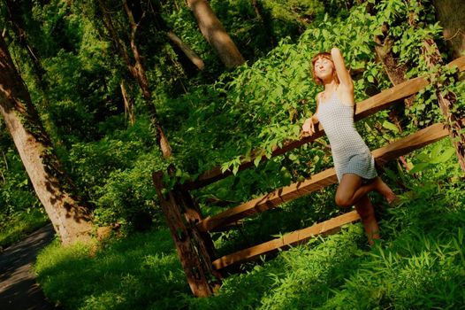 Pretty girl leaning against fence in woods.