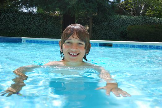 Smiling teen boy swimming in the pool surrounded with white flower bushes in the background.