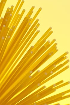 Uncooked spaghetti detail on yellow background.