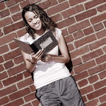 Beautiful young girl reading notebook against a brick wall.