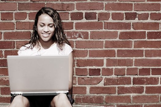 Pretty young woman using a laptop against a brick wall.