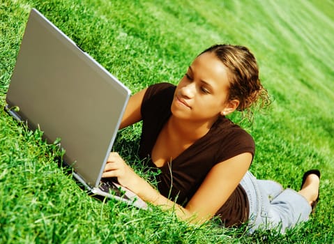 Beautiful young woman typing on a laptop in a green field.