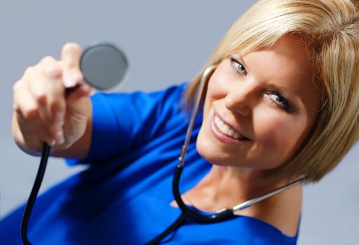 Mature woman nurse in scrubs holding up stethoscope.