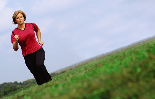 Mature woman jogging in a big summer field.