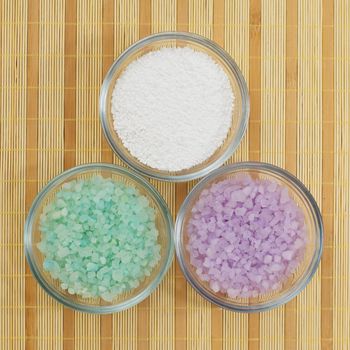 Color bath salts in bowls, on display against a bamboo mat.
