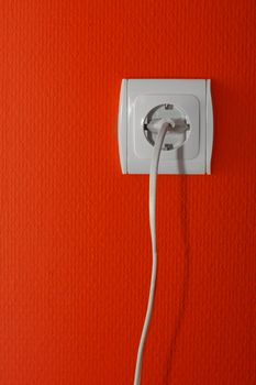 Electric outlet on a red wall, cable connected