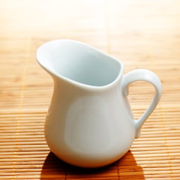 White pitcher on display against a bamboo mat.