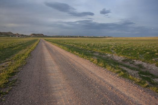 dirt farm road in Pawnee Grassland, northern Colorado, high cliffs. farm buildings and wind turbine at horizon