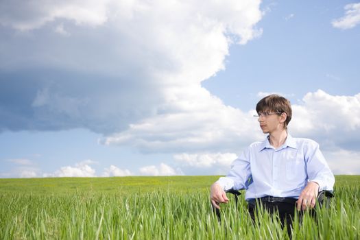 Businessman sitting on green grassland under blue sky