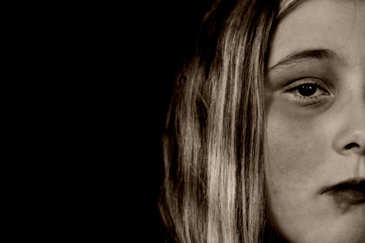 A young girl looking sullen because of child abuse and depression, isolated against a black background