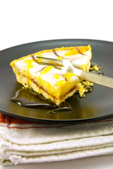 delicious looking iced bakewell tart on a black plate with a treacle drizzle and a fork on a plain background