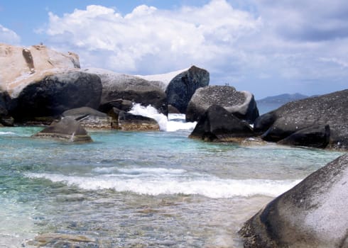 Waves crashing against large granite boulders on the beach of a paradise island.         