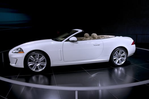 This is an expensive white convertible with a tan interior on display at the auto show with the top down.
