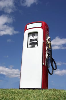 A vintage antique Gasoline fuel pump sitting on a grassy hill against the blue sky.