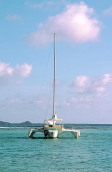 A Trimaran sailboat anchored in the bay of a paradise island setting.