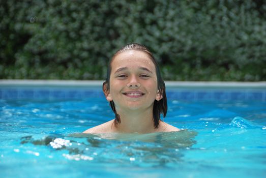 Smiling teen boy in swimming pool surrounded with white flower bushes in the background.