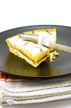 delicious looking iced bakewell tart on a black plate with a fork and a plain background