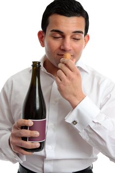 A man sniffing the cork of a bottle of wine.  White background.