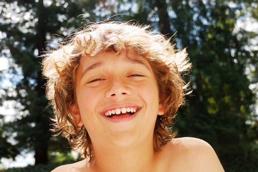 Smiling teen boy enjoying summer against blurry tree and sky background.