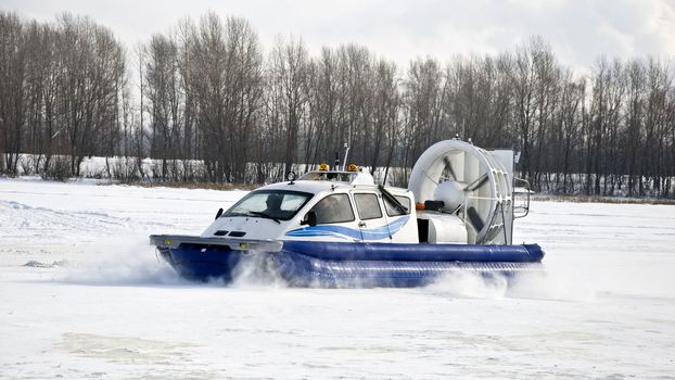 Hovercraft rides on the frozen river, picking up snow dust. Winter