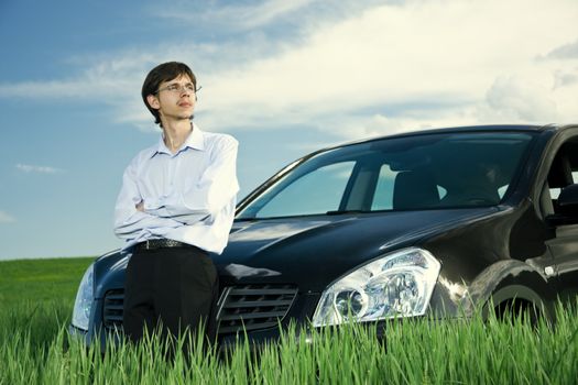 Successful businessman with car on green grassland under blue sky