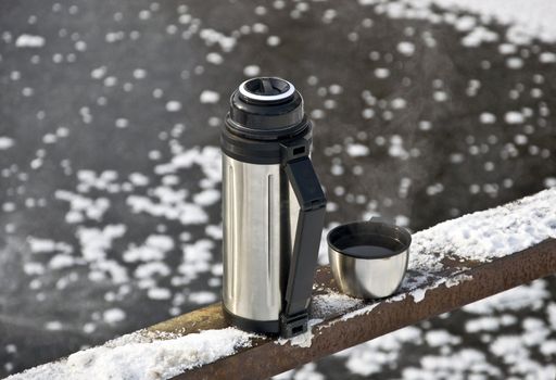 Metal thermos with hot tea drink. Winter.