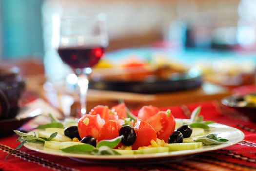 Greek salad with tomato, cucumbers and black olives, a glass of red wine in the background