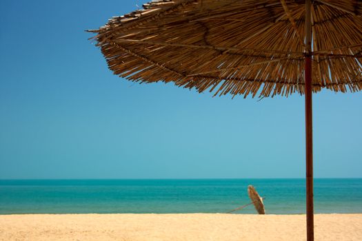 Tropical beach with blue sea water, golden sands, blue sky and parasols.