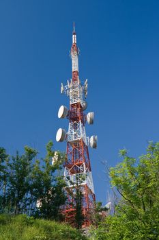 Telecommunication tower between trees above the town. The photo is taken with use of circular polarizer 