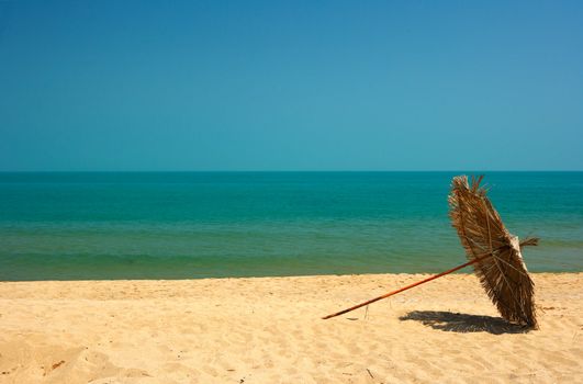 Beach with deep blue sea water, golden sands and a parasol