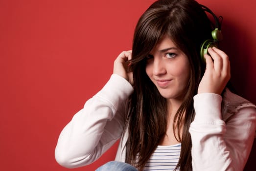 Young girl listening music with headphones on a red wall