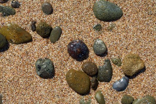 Colorful wet stones on a beach sand