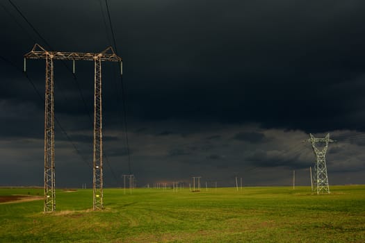 Landscape with dark storm clouds, green field and high voltage electricity poles