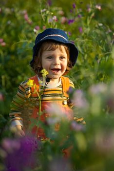 Little boy in a flowers field smiling at sunset light