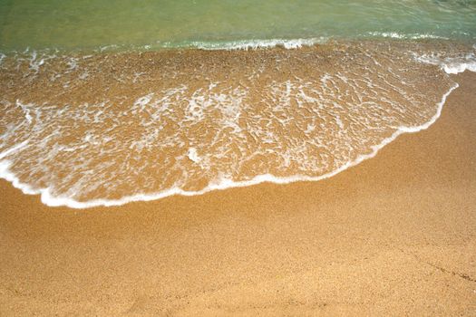 A wave, splashing on golden beach sand