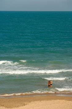 Two girls wade into water at a tropical beach with blue water