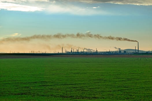 A field with an oil refinery on the horizon