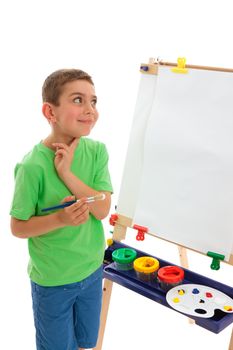 A young boy child stands by his easel and contemplates what do paint.  White background.