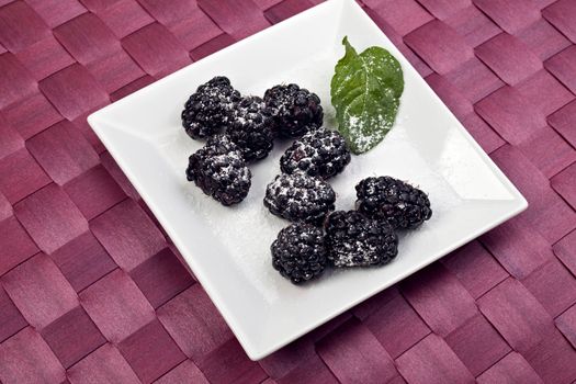 blackberries on a white plate with a peppermint leaf