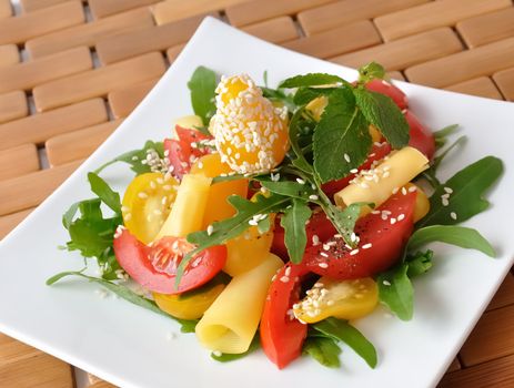 Salad of red and yellow tomato with cheese, arugula, sesame