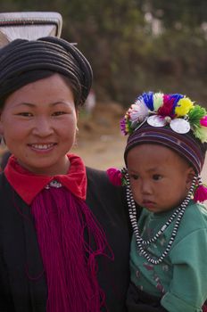 Woman wearing the headdress of black ethnic Dao Tien. She is dressed all in black. Her hair is made of braided rope dyed black hair attached to two aluminum rods that pass through the bun inside. An aluminum cone is hammered elements overcomes the cap. Typical women Dao Tien
Her baby is a cute little cap Multicolor